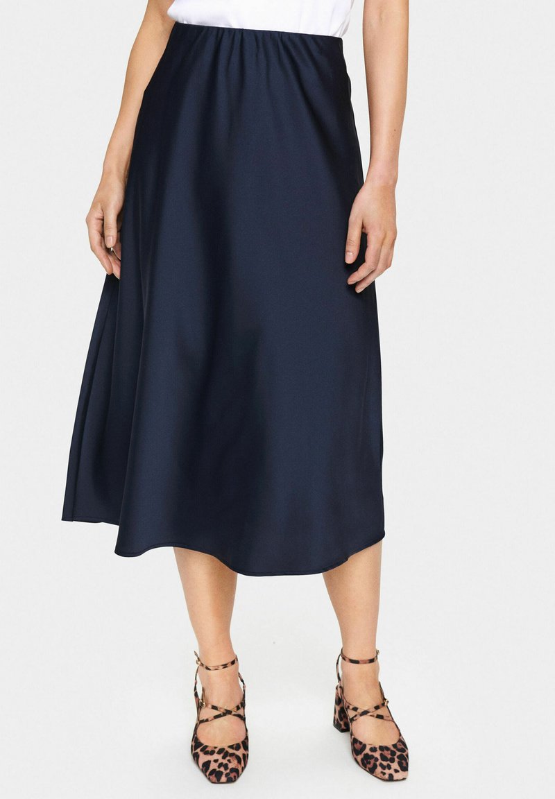 Jupe midi en satin bleu marine avec taille élastique et design fluide, associée à des escarpins à imprimé léopard avec des brides de cheville.