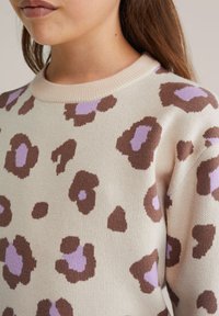 Pull en maille présentant une base crème avec des taches de léopard marron et lavande. Conçu avec un col rond côtelé et une texture douce.