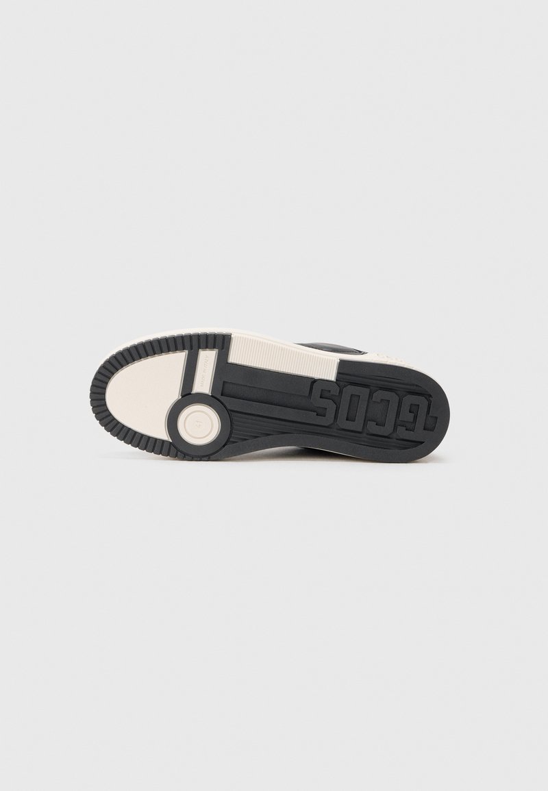 Black and cream sneaker sole featuring rubber material, textured grip, circular feature, and embossed brand logo for traction.