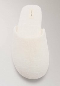 Bela teksturirana tkanina copat z zaprtim zaobljenim nosom in mehkim podplatom, fotografirana z vrha na nevtralni podlagi.