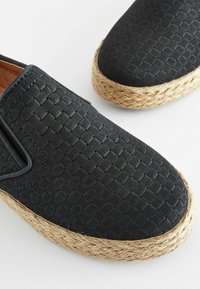 Schwarze geflochtene Slipper mit strukturiertem Obermaterial, ausgestattet mit einer Espadrille-artigen Jutesohle und blauen Nähakzenten.