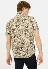 Kurzarmhemd aus leichtem Stoff, mit einem beigen und schwarzen geometrischen Muster, spitzem Kragen und abgerundetem Saum.