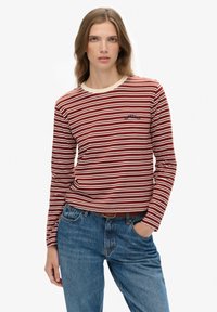 Langermige shirt met rood-witte horizontale strepen, roomkleurige kraag en een klein geborduurd detail op de borst, gecombineerd met blauwe jeans.