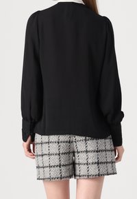 Czarna bluzka z długim rękawem ze ściąganymi ramionami, w połączeniu z szaro-czarnymi kratkowymi szortami z tkaniny o teksturowanej fakturze i frędzlami na brzegu.