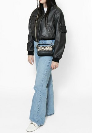 Zwarte leren bomberjack met geribbelde manchetten, lichtblauwe flared jeans en een crossbody tas met luipaardprint. Witte instappers met een accentgesp.
