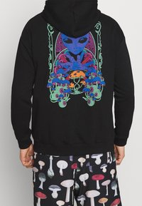 Schwarzer Hoodie mit einem farbenfrohen Alien-Design, auf dem Rücken mit Pilzen und komplexen Mustern. Die Vorderseite ist schlicht mit einem abgerundeten Saum.