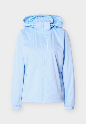 Lys blå hettejakke med glidelås foran, elastiske mansjetter, glidelåslommer på sidene, og vertikalt hvitt Calvin Klein-logo på brystet.