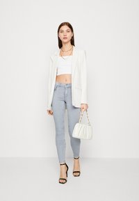 Blazer blanco a rayas, top corto blanco, jeans ajustados azul claro, tacones altos negros con tiras y un bolso acolchado blanco con cadena dorada.