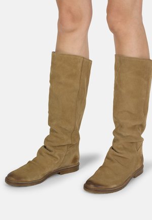 Botas de ante color beige hasta la rodilla con un diseño arrugado, suelas planas y textura suave. Presentan una punta redondeada y detalles de costura mínimos.