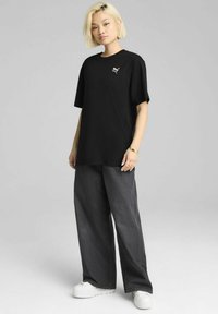 Maglietta nera a maniche corte con un piccolo logo, abbinata a pantaloni grigi larghi e sneakers bianche chunky. Design semplice e casual.