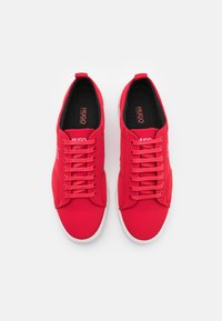 Rote Leinenschuhe mit runden Zehen, Schnürsenkeln und weißen Gummisohlen. Verfügt über Branding auf der Zunge und der Seite. Insgesamt glatte Textur.