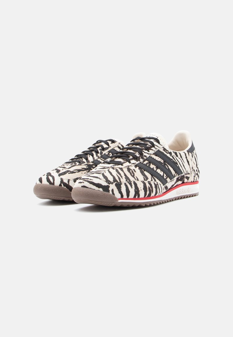 White and black zebra-striped sneakers with round toe, lace-up design, textured suede upper, featuring three black stripes and a red accent.