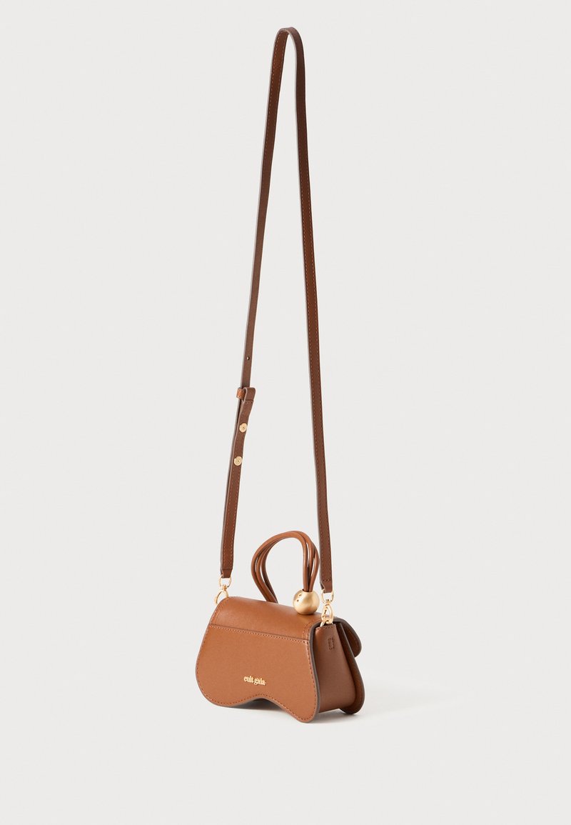 Sac à main en simili cuir brun avec une forme unique, des finitions dorées, une longue bandoulière et un détail de poignée supérieure arrondie.