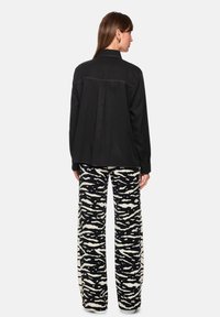 Black shirt with a collar and back pleat, paired with wide-leg pants featuring a black and white abstract pattern.
