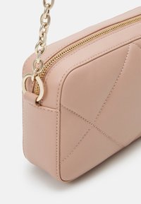 Pochette en cuir rose clair avec couture losange, fermeture éclair dorée et bandoulière chaîne dorée attachée par un anneau rond.