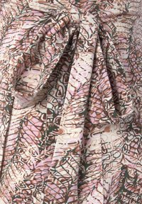 Patterned fabric featuring abstract floral designs in pink, brown, and green. Includes a tied detail and soft, textured cotton material.