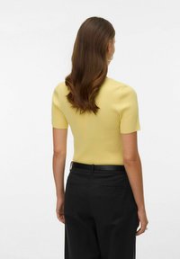 Geel geribd gebreid topje met korte mouwen, aansluitend model, gedragen met zwarte high-waisted broek met zijzakken en een riem.