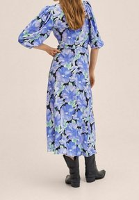 Květinové midi šaty s velkými modrými a zelenými květinami na černém pozadí, nabírané rukávy a zvýrazněný pas. Doplněno černými botami.