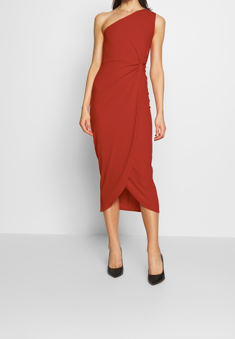 Asymmetrisk röd klänning med en axel, tillverkad av mjukt tyg, med en vriden knutdetalj vid midjan och en wrapkjol i knähöjd.