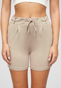Pantaloni corti beige realizzati in tessuto morbido, con vita regolabile tramite cordoncino con estremità in metallo e pinces frontali, aderenti alle cosce.