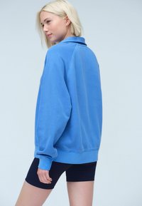 Blauw oversized sweatshirt met kraag, geribde manchetten en zoom. Gekocht met zwarte fietsbroekjes. Zacht katoen materiaal, casual ontwerp.