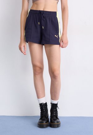 Navy blue athletic shorts with light yellow side panels, drawstring waist, and gold logo detail, paired with black lace-up boots and white socks.