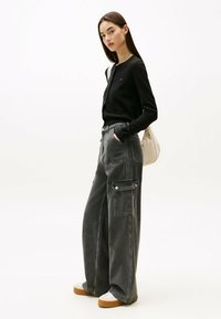 Cardigan negro de manga larga con cierre de botón, combinado con pantalones cargo grises sueltos con bolsillos laterales, y zapatillas blancas con suelas beige.