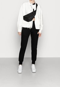 Vit jacka, svarta sweatpants med logotyp, svart crossover-väska och vita sneakers. Outfiten har en avslappnad passform och minimalistisk design.