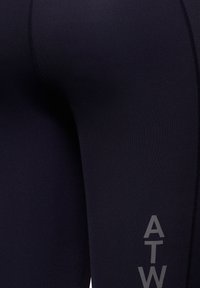 Czarne legginsy sportowe wykonane z elastycznego materiału, z gładką fakturą i nadrukowanym szarym logo "ATW" po boku.