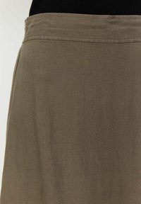 Una gonna semplice, lunga fino al ginocchio, di un verde oliva tenue, realizzata in un morbido tessuto testurizzato con una vita semplice.