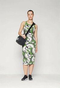 Vestido bodycon verde com um padrão de penas brancas, combinado com ténis pretos e uma mala cruzada preta, realçando uma silhueta justa.