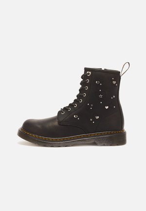 Botte en cuir noir à lacets avec des surpiqûres jaunes, décorée de petits clous argentés en forme de cœur et d'étoile sur le panneau latéral.