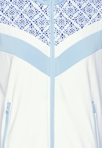 Lehká zipová bunda s bílým tělem, modrými akcenty a horní částí s květinovým vzorem. Obsahuje dvě boční kapsy.