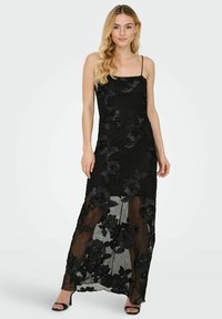 Juoda maxi suknelė su plonais dirželiais, puošta gėlių nėrinių siuvinėjimu, permatoma apatine dalimi ir prigludusiu liemeniu. Lygi tekstūra.
