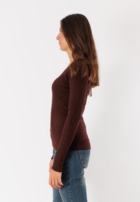 Top lungo a maniche ribatte con scollatura a V e dettaglio con fiocco sul retro, abbinato a jeans in denim. Il tessuto sembra morbido e ha una silhouette aderente.