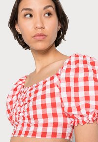 Top crop xadrez vermelho e branco com mangas bufantes, detalhe franzido na frente e decote quadrado. O tecido parece leve e texturizado.