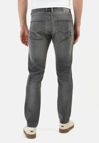 Jean en denim gris à coupe slim, comportant des poches arrière et un léger dégradé. Associés à des baskets blanches et à une simple chemise blanche.