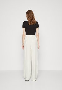 Top corto negro de manga corta combinado con pantalones de pierna ancha de talle alto color crema, con un tejido texturizado y cinturilla elástica.