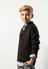 Brązowy sweter z prążkowanego dżerseju z zapięciem na guziki dwurzędowe, w połączeniu z jasnoszarą koszulą z kołnierzykiem i szarymi spodniami w wzory.