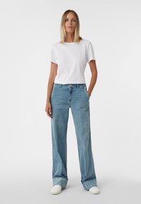 Biała bawełniana koszulka zestawiona z jasnoniebieskimi szerokimi jeansami o luźnym kroju i podwiniętych nogawkach, uzupełniona białymi tenisówkami.