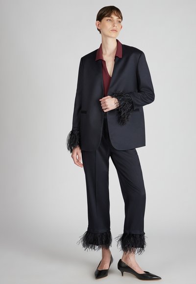 Czarna marynarka z piórowymi mankietami, zestawiona z ciemnymi spodniami. Głęboki burgundowy top pod spodem oraz czarne czółenka z ostrym noskiem. Gładka faktura tkaniny.