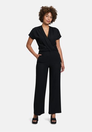Schwarzer Jumpsuit mit kurzen Ärmeln, tiefem V-Ausschnitt und weitem Bein. Glatter Stoff mit taillierter Passform, der subtile Drapierungsdetails aufweist.