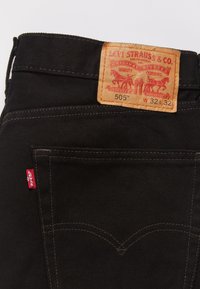 Črne jeans hlače Levi's z zadnjim žepom, rdeča oznaka Levi's in svetlo rjava usnjena nalepka, ki prikazuje velikost W32 L32 in model 505.