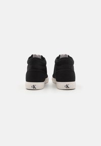Svarta kanvas högsnörade sneakers med en solid design, vita gummisålar och logodetalj på hälen. Sömmen synlig på ovansidan.