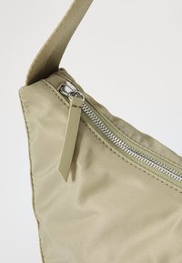 Borsa in nylon verde morbido con una forma diagonale, dotata di una cerniera argentata e un occhiello in tessuto. Spallaccio robusto per il trasporto.