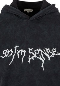 Juodas gobtuvėlis iš minkštos medžiagos, frontinėje dalyje turintis didelį baltą grafikos tekstą. Įrengtas su raišteliu reguliuojamu gobtuvu ir tekstūruotu paviršiumi.