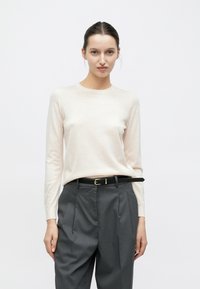 Maglione rosa chiaro a maniche lunghe realizzato in tessuto morbido, abbinato a pantaloni grigi pieghettati a vita alta e cintura nera con fibbia dorata.