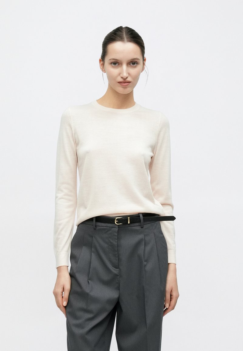 Maglione rosa chiaro a maniche lunghe realizzato in tessuto morbido, abbinato a pantaloni grigi pieghettati a vita alta e cintura nera con fibbia dorata.