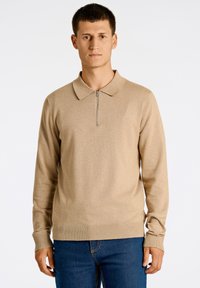Beige långärmad polotröja med dragkedja, med krage och ribbade ärmslut. Tillverkad av ett stickat tyg med en subtil textur.