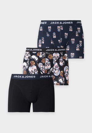 Høj, slank mand iført sorte Jack & Jones boxershorts står barfodet mod en ensfarvet hvid baggrund og kigger til højre med den ene hånd bag ryggen.